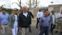 Presiden AS Donald Trump dan ibu negara Melania Trump berkeliling ke permukiman yang terdampak Badai Maria di Guaynabo, Puerto Rico, Selasa (3/10). Akan tetapi, dalam kunjungan itu Melania terlihat menggunakan celana jins berwarna putih. (MANDEL NGAN/AFP)