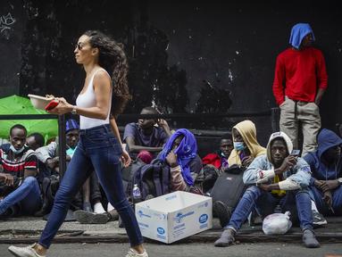 Pejalan kaki melewati para migran yang menunggu dalam antrean di luar The Roosevelt Hotel yang digunakan oleh kota sebagai tempat tinggal sementara, Senin, 31 Juli 2023, di New York. (AP Photo/John Minchillo)