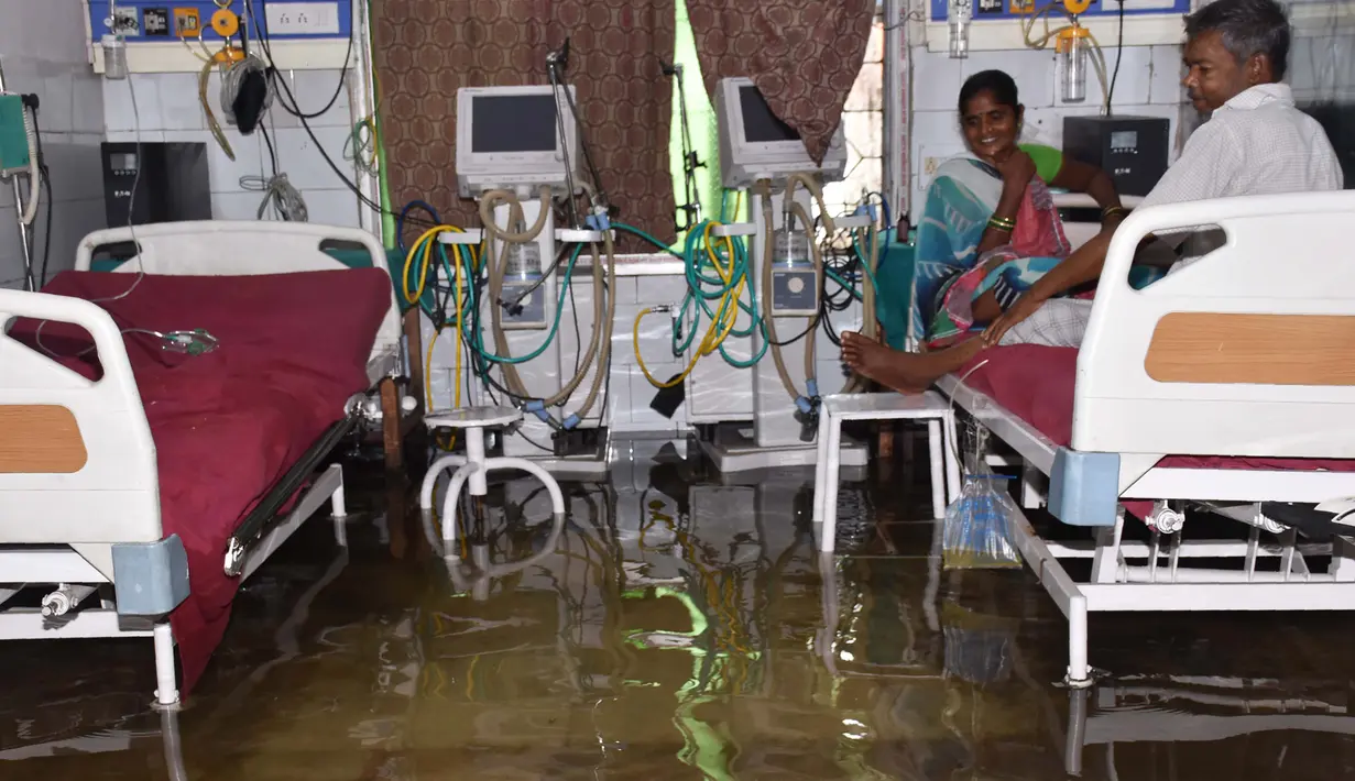 Pasien dan anggota keluarganya berada di dalam bangsal yang tergenang banjir di Nalanda Medical College Hospital, daerah Bihar, India, 29 Juli 2018. Rumah sakit itu digenangi air kotor dengan sejumlah ikan terlihat berenang memenuhi lantai. (AFP PHOTO)