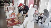Pelayan membersihkan meja yang diberi pembatas banner bergambar karakter di KFC Salemba, Jakarta, Selasa (23/6/2020). Banner bergambar tersebut berguna untuk pembatas bagi pengunjung yang makan di tempat saat fase kenormalan baru. (Liputan6.com/Faizal Fanani)