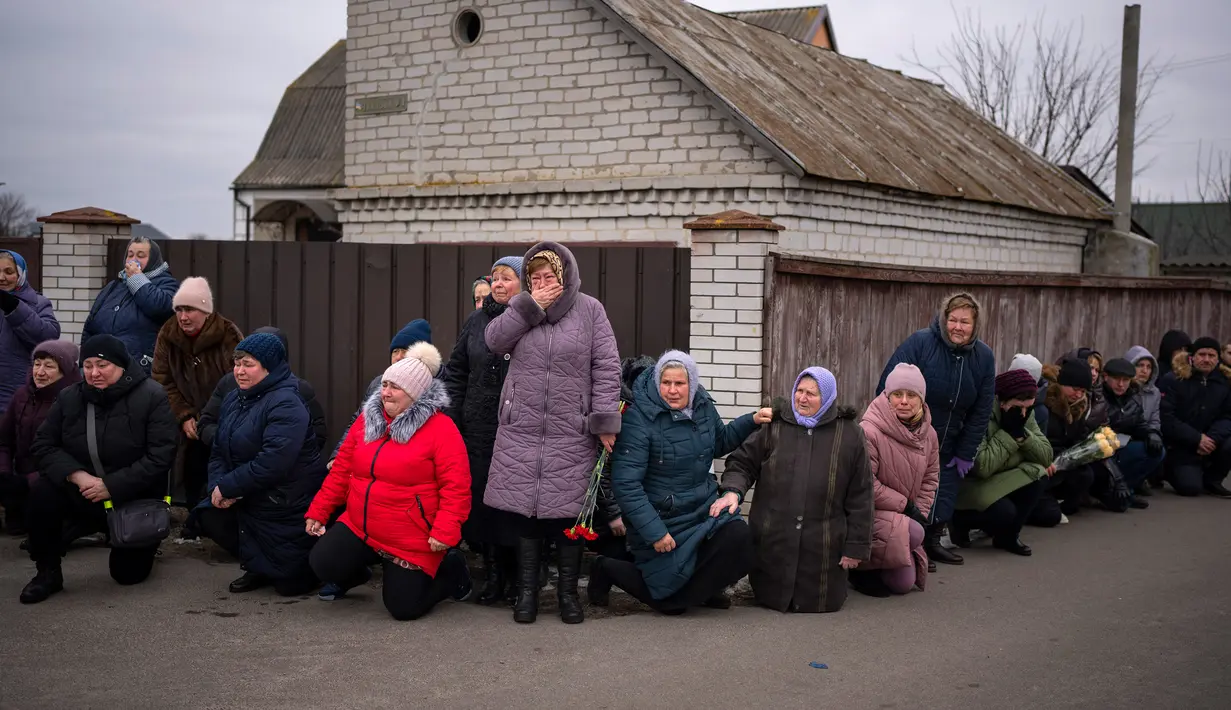 Para pelayat berlutut menunggu peti mati Oleksandr Maksymenko (38) lewat saat pemakamannya di kampung halamannya di Kniazhychi, sebelah timur Kyiv, Ukraina, 13 Februari 2023. Oleksandr Maksymenko, seorang warga sipil yang menjadi sukarelawan di angkatan bersenjata Ukraina, tewas dalam pertempuran di daerah Bakhmut. (AP Photo/Emilio Morenatti)