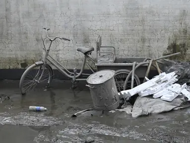 Sebuah sepeda roda tiga yang tertutup lumpur terlihat di dekat rumah seorang warga setelah banjir akibat hujan lebat di kota Zhuozhou, di provinsi Hebei, China utara, Rabu (9/8/2023). (Jade Gao / AFP)