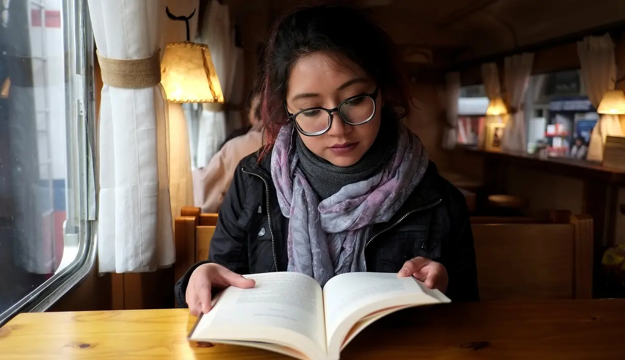 Pengunjung membaca buku di sebuah kafe yang dibangun dari gerbong kereta tua di La Paz, Bolivia pada 15 Maret 2019. Selain dimanfaatkan sebagai kafe, bagian gerbong kereta juga dijadikan toko yang menjual produk makanan dan minuman (David Mercado/Reuters)