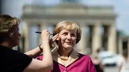 Seorang seniman merapikan dandanan patung lilin Angela Merkel, di depan gerbang Brandenburg di Berlin, (16/7/2014). (AFP PHOTO/Clemens Bilan)