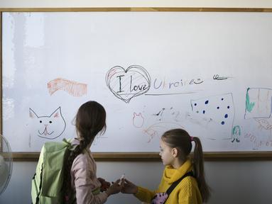 Dua anak pengungsi dari Ukraina berdiri di depan papan tulis sebelum kelas mereka dimulai di Berlin, Jerman, Senin, 21 Maret 2022. Empat puluh anak pengungsi Ukraina memulai hari pertama mereka di sekolah dasar di Berlin pada Senin hanya beberapa minggu setelah mereka melarikan diri dari perang pula