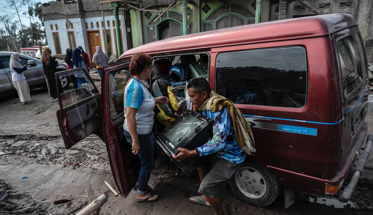 Seorang warga menyelamatkan barang-barang miliknya dari rumahnya yang rusak di desa Curah Kobokan di Lumajang, Jawa Timur, Rabu (8/12/2021). Akibat erupsi Gunung Semeru, sebagian besar rumah di desa tersebut runtuh. (Juni Kriswanto / AFP)