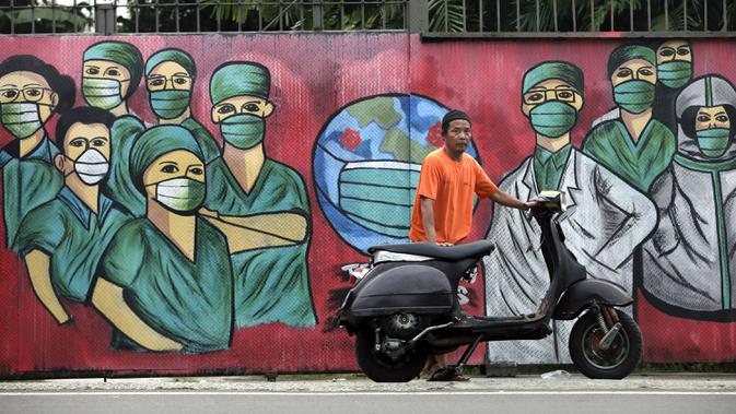 Seorang pengendara sepeda motor berhenti dekat mural yang dibuat sebagai penghormatan terhadap petugas medis yang sedang melawan virus corona COVID-19 di Depok, Jawa Barat, Indonesia, Rabu (15/4/2020). (AP Photo/Dita Alangkara)