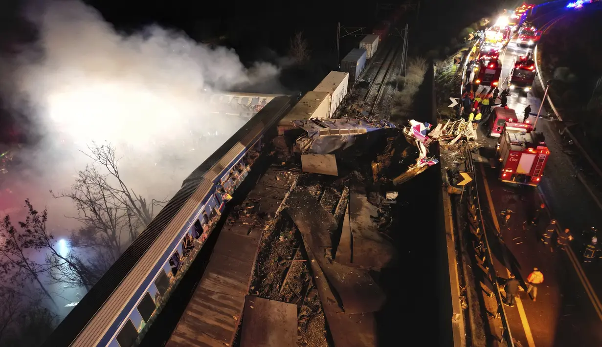 Asap mengepul dari kereta saat petugas pemadam kebakaran dan penyelamat beroperasi setelah tabrakan di dekat kota Larissa, Yunani, Rabu dini hari (1/3/2023). Tabrakan antara kereta barang dan penumpang terjadi di dekat Tempe, sekitar 380 kilometer (235 mil) utara Athena, dan mengakibatkan anjloknya beberapa gerbong kereta. (AP Photo/Vaggelis Kousioras)