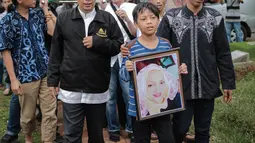 Cucu aktris senior Titi Qadarsih membawa pigura foto sang nenek saat akan dimakamkan di TPU Tanah Kusir, Jakarta, Selasa (23/10). Kabar meninggalnya Titi pertama kali disiarkan oleh anaknya, Indra Qadarsih. (Liputan6.com/Faizal Fanani)