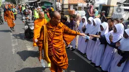 Para murid sekolah dasar berdiri di pinggir jalan raya sambil menyemati para Biksu. Selain murid SD, para Biksu juga disamut warga setempat dan umat dari agama lain. (merdeka.com/Arie Basuki)