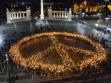 Orang-orang membuat tanda perdamaian dengan lampu saat demonstrasi untuk Ukraina yang diselenggarakan oleh Greenpeace di Heroes Square, Budapest, Hungaria, 9 Maret 2022. Invasi Rusia ke Ukraina telah memicu migrasi massal terbesar di Eropa dalam beberapa dekade. (AP Photo/Anna Szilagyi)
