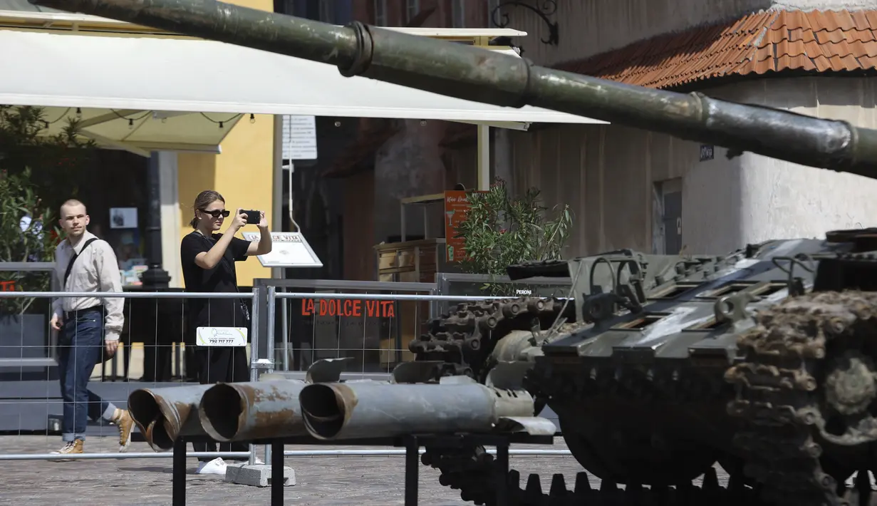 Seorang wanita menggunakan ponselnya mengabadikan tank Rusia yang rusak dan terbakar di Castle Square, di Warsawa, Polandia (27/6/2022). Pihak berwenang Ukraina mengumumkan bahwa ada rencana untuk pameran serupa di ibu kota Eropa lainnya seperti Berlin, Paris, Madrid dan Lisbon. (Foto AP/Michal Dyjuk)