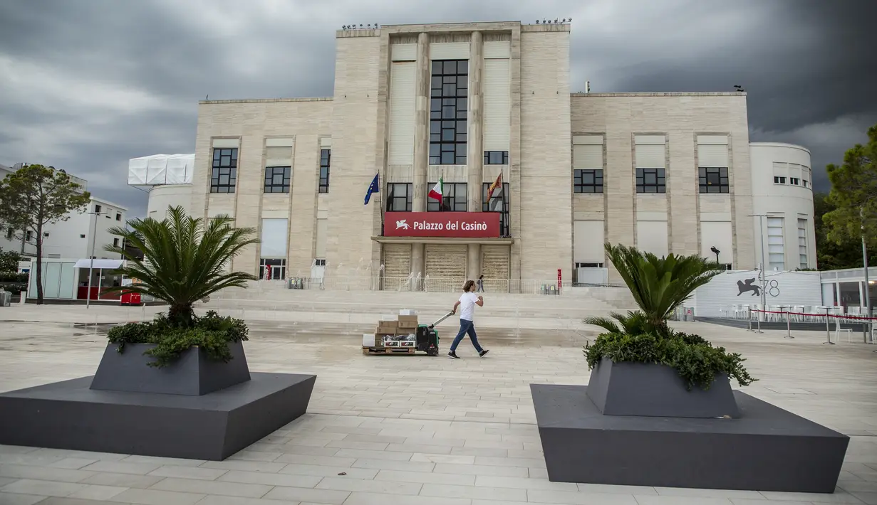 Seorang pekerja membawa komoditas di depan bekas gedung kasino Venice Lido sehari sebelum dimulainya Festival Film Venesia edisi ke-78 di Venice Lido, Italia, Selasa (30/8/2021).  Festival ini berlangsung dari 1 hingga 11 September. (Photo by Joel C Ryan/Invision/AP)