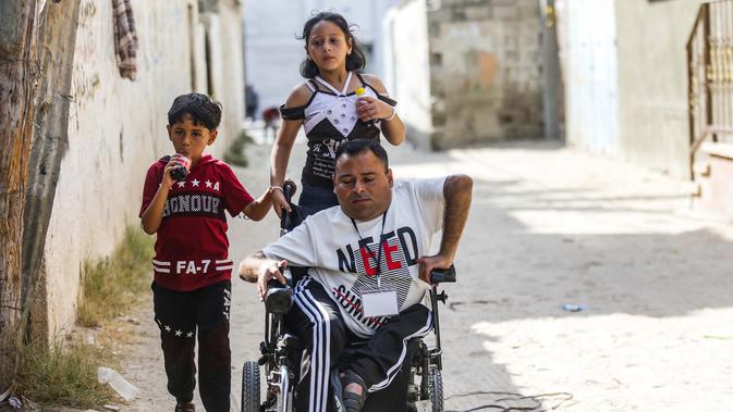 Nihad Jarboa (37) bergerak dengan kursi roda ditemani oleh anak-anaknya Rahaf (kanan), 10, dan Eyad, 7, di sepanjang jalan di kamp pengungsi Rafah di Jalur Gaza selatan, pada 21 Juli 2020. (AFP Photo/Said Khatib)