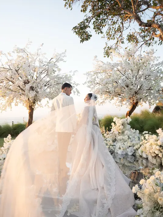 Untuk menyempurnakan penampilannya, Jennifer mengenakan veil panjang beraksen lace floral yang membingkai wajahnya dengan lembut. Detail renda pada tepian veil berpadu harmonis dengan motif lace pada gaun, menciptakan tampilan bridal yang elegan dan timeless. [@jennifercoppenreal20].
