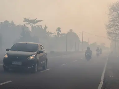 Para pengendara bermotor menyalakan lampu depan kendaraan saat melintasi jalan yang diselimuti kabut asap di Kota Palangka Raya, Kalimantan Tengah, Kamis,  20 Agustus 2026. (AFP/ Reina)