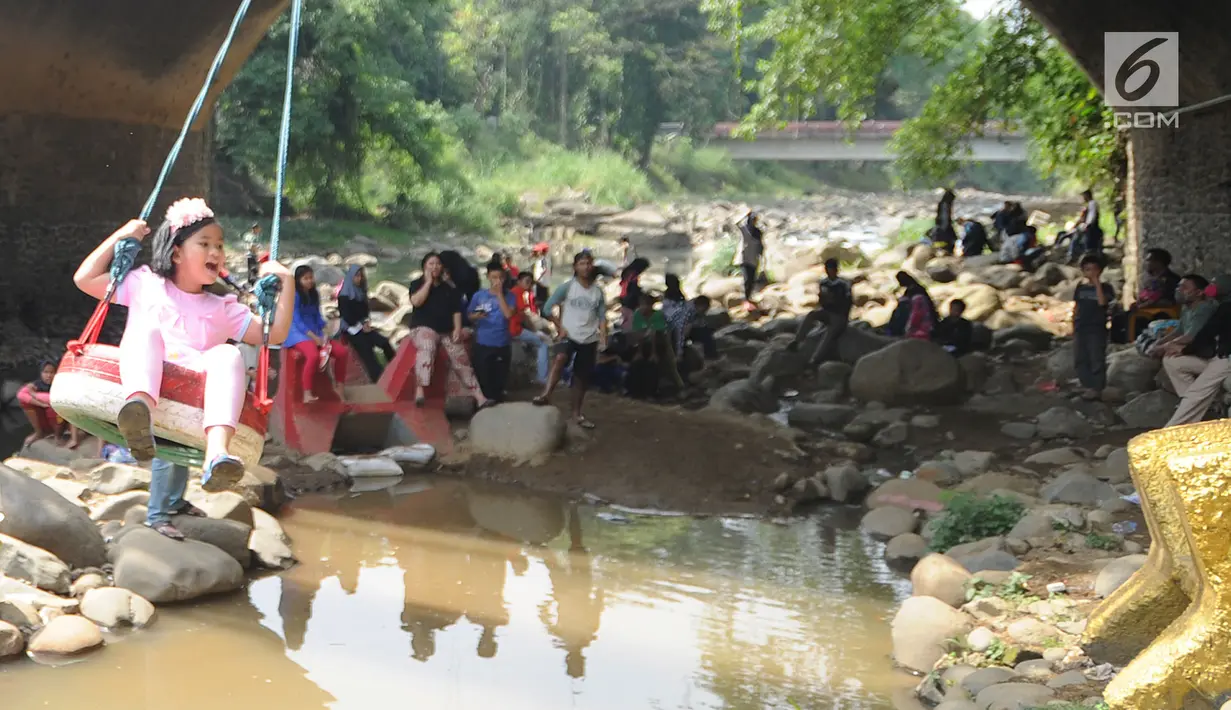 Seorang anak bermain ayunan di kolong jembatan Sempur, Bogor (16/9). Musim kemarau yang menyebabkan debit Sungai Ciliwung menyusut drastis dimanfaatkan warga Bogor dan sekitarnya untuk berwisata murah dan gratis di aliran sungai. (Merdeka.com/Arie Basuki)