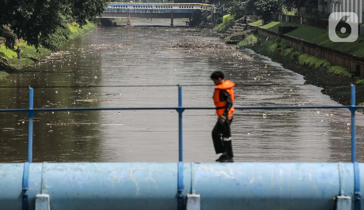Suasana Kali Ciliwung saat seorang petugas PPSU berjalan menyusuri pipa, Jakarta, Rabu (19/5/2021). Petugas PPSU membersihkan sampah yang tersangkut di tengah derasnya aliran Kali Ciliwung agar tidak ada penumpukan dan sedimentasi. (Liputan6.com/Faizal Fanani)