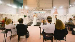 Pengunjung mengamati model yang memperagakan gaun pengantin di pameran dagang European Bridal Week di Essen, Jerman, pada 5 Juli 2020. European Bridal Week diselenggarakan dengan menerapkan langkah pengendalian dan pencegahan COVID-19 yang ketat. (Xinhua/Tang Ying)