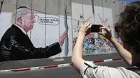 Seorang pengendara motor melintas didepan grafiti yang menggambarkan Presiden AS Donald Trump di tembok pemisah Israel - Palestina di kota Bethlehem (4/8). (AFP Photo/Musa Al Shaer)