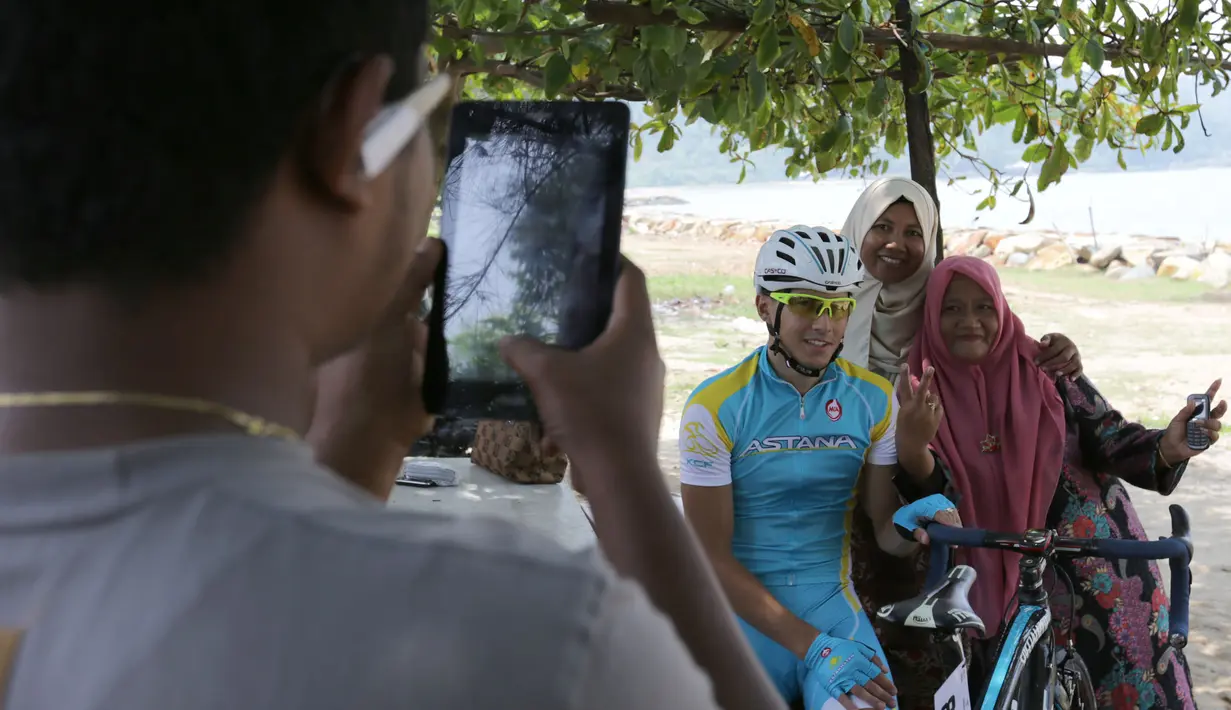 Warga sekitar Pantai Carocok berfoto bersama seorang pebalap sepeda berlomba dalam Etape 1 Tour de Singkarak antara Painan, Kabupaten Pesisir Selatan menuju Pariaman, Sumatra Barat saat, Sabtu (3/10/2015). (Bola.com/Arief Bagus)