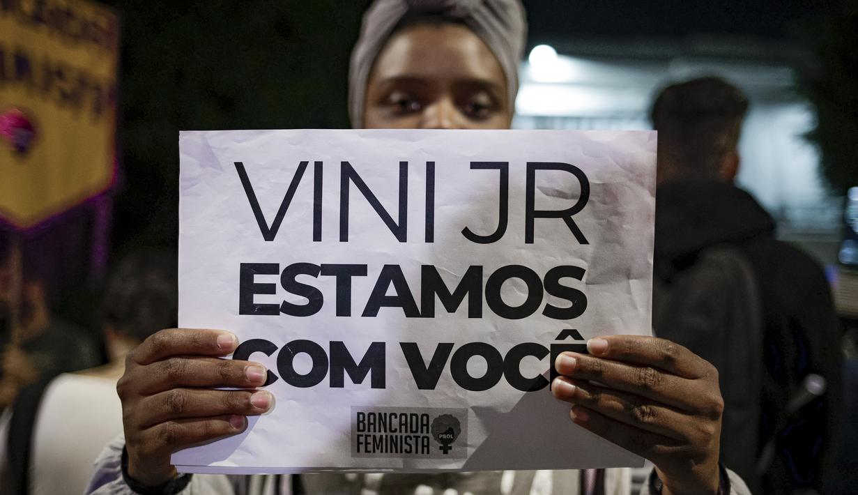 Seorang perempuan memegang tanda dengan pesan yang berbunyi dalam bahasa Portugis; "Vini, kami bersamamu," saat memprotes serangan rasis yang dialami pemain Real Madrid asal Brasil, Vinicius Jr., di luar Konsulat Spanyol di Sao Paulo, Brasil, Selasa (23/5/2023). (AP Photo/Tuane Fernandes)