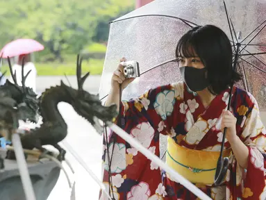 Seorang wanita mengenakan  yukata, pakaian musim panas tradisional Jepang dan masker untuk melindungi diri dari virus corona mengambil foto di lingkungan Asakusa di Tokyo, Jumat (13/8/2021). Yukata adalah jenis kimono yang dibuat dari bahan kain katun tipis tanpa pelapis. (AP Photo/Koji Sasahara)