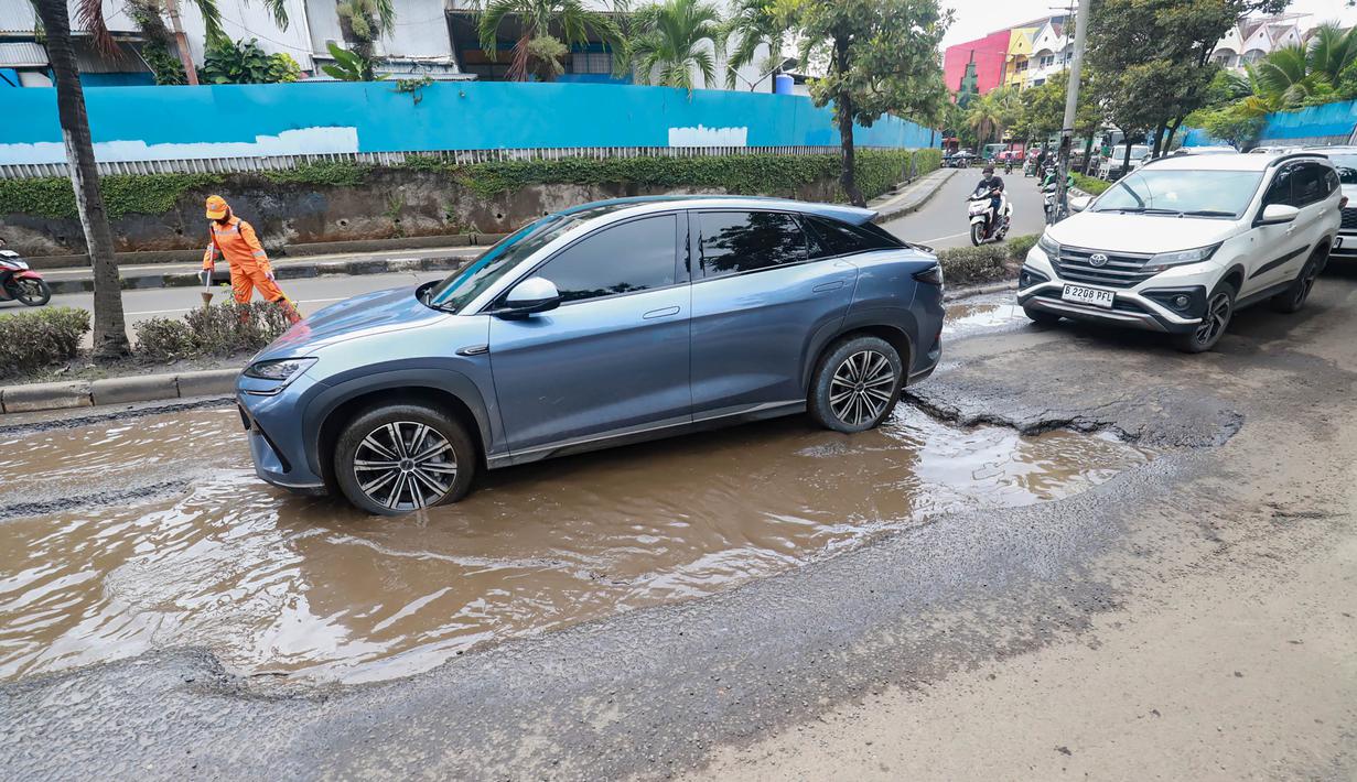 Pengendara kendaraan roda dua dan roda empat terpaksa harus memperlambat laju kendaraan untuk menghindari kerusakan jalan dan mencegah terjadinya kecelakaan lalu lintas. Tampak dalam foto, sejumlah pengendara melewati kerusakan di Jalan Mitra Bahari, Penjaringan Jakarta Utara, Selasa (3/2/2026). (merdeka.com/Arie Basuki)