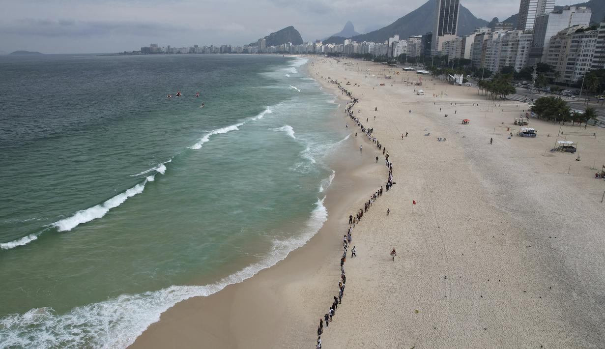 Orang-orang membuat garis di sepanjang pantai Copacabana pada Hari Laut Sedunia di Rio de Janeiro, Brasil, Rabu (8/9/2022). Organisasi Route Brasil menyerukan agar orang-orang berkumpul untuk acara yang diberi nama "Pelukan Itu," dan untuk memungut sampah di pantai, untuk menarik perhatian pada pencemaran laut. (AP Photo/Silvia Izquierdo)