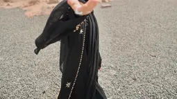 Dinda tampak memadukan abaya hitam polos dengan outer berhiaskan payet di tepiannya. Penampilannya dilengkapi dengan kacamata hitam. (Instagram/dindahw).
