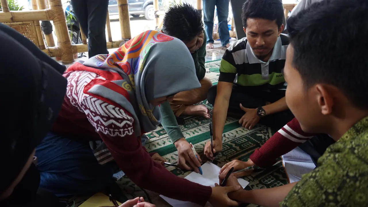 Peserta Sekolah Damai melakukan interaksi berupa menggambar di atas sehelai kertas dengan mata ditutup oleh kain
