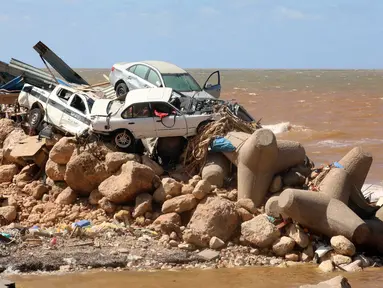 Mobil bertumpuk di atas pemecah gelombang dan puing-puing bangunan yang hancur akibat banjir bandang setelah badai Mediterania "Daniel" menghantam kota Derna di timur Libya, Kamis (14/9/2023). (Abdullah DOMA / AFP)