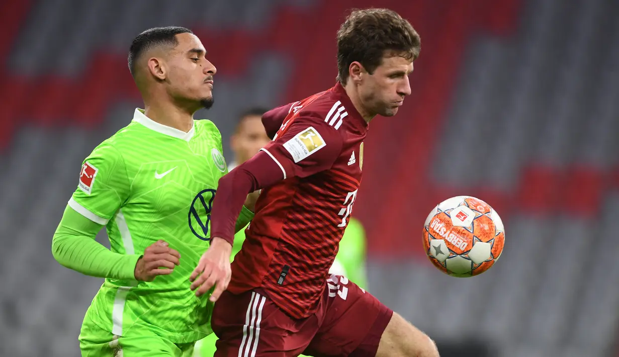 Bek VfL Wolfsburg Maxence Lacroix (kiri) berebut bola dengan pemain depan Bayern Munchen Thomas Mueller pada pekan ke-17 Liga Jerman di Allianz Arena Sabtu (18/12/2021) dinihari WIB. Bayern mencukur Wolfsburg dengan skor 4-0. (Christof STACHE / AFP)
