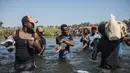 Para migran menyeberangi Rio Grande dari Del Rio, Texas, ke Ciudad Acuña, Meksiko, untuk berbelanja makanan sebelum kembali ke sisi perbatasan AS, Minggu (19/9/2021). Ribuan migran Haiti telah tiba di Del Rio, Texas, saat pihak berwenang berupaya menutup perbatasan.(AP Photo/Felix Marquez)