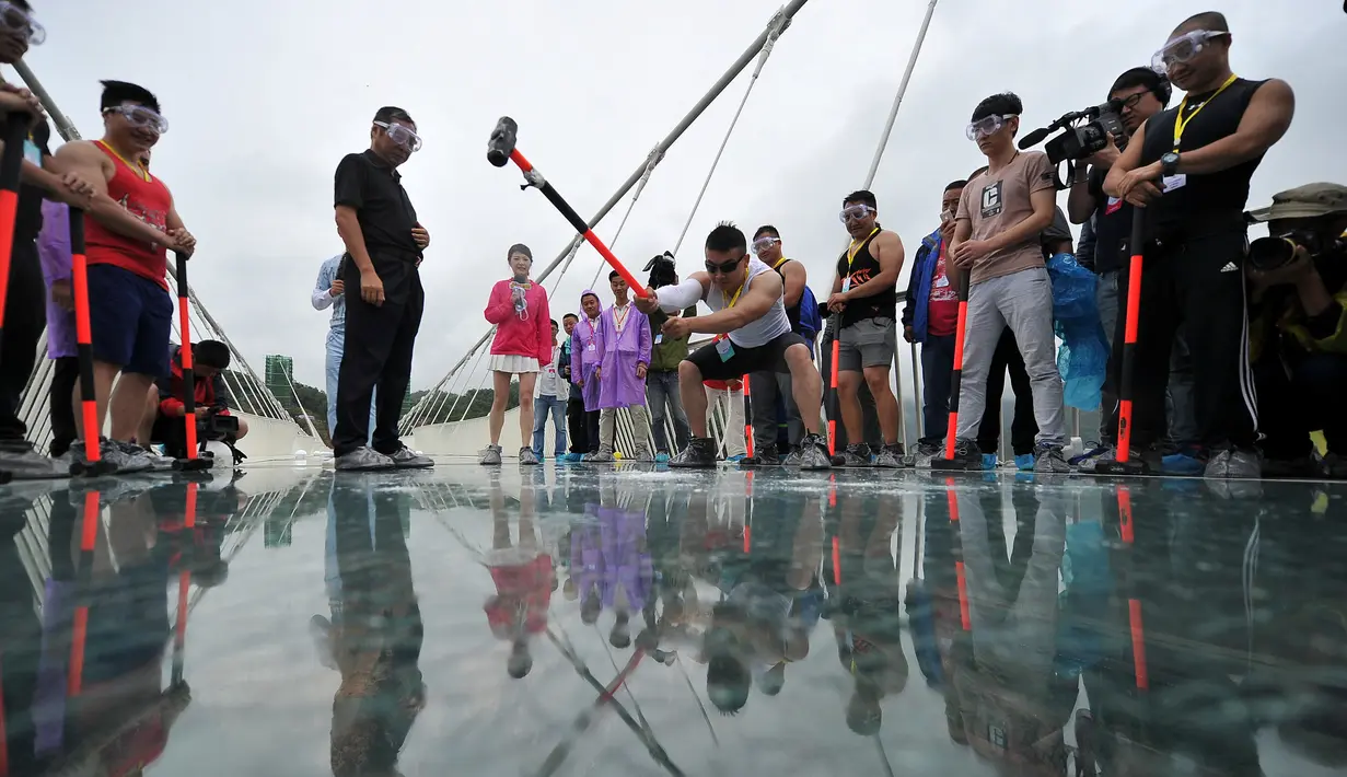 Seorang pria memukulkan palu untuk mengukur kekuatan jembatan di Provinsi Hunan, Cina, (25/6). Ini dilakukan untuk mengetahui keamanan yang dimiliki oleh jembatan dari kaca ini. (REUTERS / Jimmy Guan)