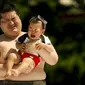 Seorang pegulat sumo amatir ikut menangis saat dia  menggendong bayi yang juga menangis di Tokyo, Jepang, (30/5/2015). Kontes ini merupakan kontes untuk suara bayi dengan tangis yang paling kencang. (REUTERS/Thomas Peter)