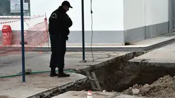 Seorang polisi mengamati sebuah lubang ditemukannya bom dari masa Perang Dunia II di Kota Thessaloniki, Yunani, 9 Februari 2017. Penemuan bom yang mengandung sekitar 250 kg bahan peledak itu memicu evakuasi sekitar 60 ribu warga. (SAKIS MITROLIDIS/AFP)