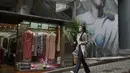 Seorang perempuan mengenakan masker berjalan di sepanjang jalan di Hong Kong, Selasa (22/3/2022). Hong Kong melaporkan 14.063 infeksi virus corona covid-19 baru pada Senin, terendah dalam lebih dari tiga minggu. (AP Photo/Kin Cheung)