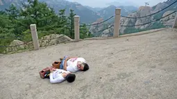 Gao Zhiyu (kiri) dan Chen Zhou merebahkan dirinya saat sampai di puncak gunung di Qingdao, Tiongkok, Selasa (13/9). Keduanya tak memiliki kaki dan menggunakan balok kayu untuk mendaki gunung setinggi 1130 meter. (REUTERS)