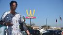 Seorang wanita berjalan dengan latar belakang plang logo restoran cepat saji McDonald's yang terbalik di Lynwood, California (8/3). Huruf W tersebut merupakan inisial untuk women atau wanita. (AFP Photo/Frederic J. Brown)