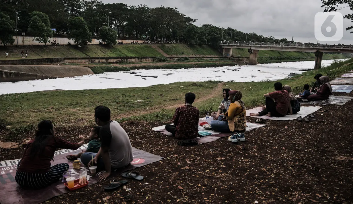 Warga bersantai di dekat limbah busa yang memenuhi aliran Kanal Banjir Timur (KBT), Duren Sawit, Jakarta, Kamis (2/7/2020). Busa yang memenuhi aliran KBT akibat limbah pabrik dan rumah tangga sejak dua minggu lalu itu menjadi tontonan warga meski menimbulkan bau tak sedap (merdeka.com/Iqbal Nugroho)