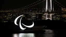 Simbol Paralimpiade menyala pada malam hari dengan latar belakang Jembatan Pelangi di tepi Pantai Odaiba, Tokyo, Jepang, 23 Agustus 2021. Paralimpiade Tokyo 2020 mulai 24 Agustus 2021 sampai 5 September 2021. (Charly TRIBALLEAU/AFP)