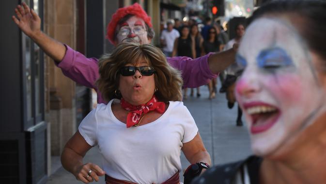 Seorang wanita berlari ketika dikejar badut dalam acara 'Running of the Clowns' di Pasadena, California pada 21 Oktober 2018. Lari dikejar kawanan badut ini merupakan parodi yang mengolok-olok lomba dikejar banteng di Pamplona, Spanyol. (Mark RALSTON/AFP)