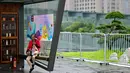 Seorang wanita memeriksa ponselnya sambil duduk di dalam stan yang dihiasi dengan poster Asian Games 2022 di sepanjang jalur pejalan kaki di sungai Qiantang di Hangzhou, provinsi Zhejiang, China pada 22 September 2023. (MANAN VATSYAYANA/AFP)