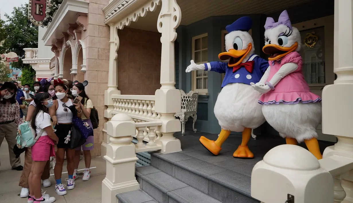 Pengunjung yang mengenakan masker berbaris untuk berswafoto dengan karakter kartun Donald Duck dan Daisy Duck di Disneyland Hong Kong pada Jumat (25/9/2020). Setelah dibuka dan tutup kembali, Disneyland Hong Kong dibuka kembali untuk wisatawan. (AP Photo/Kin Cheung)