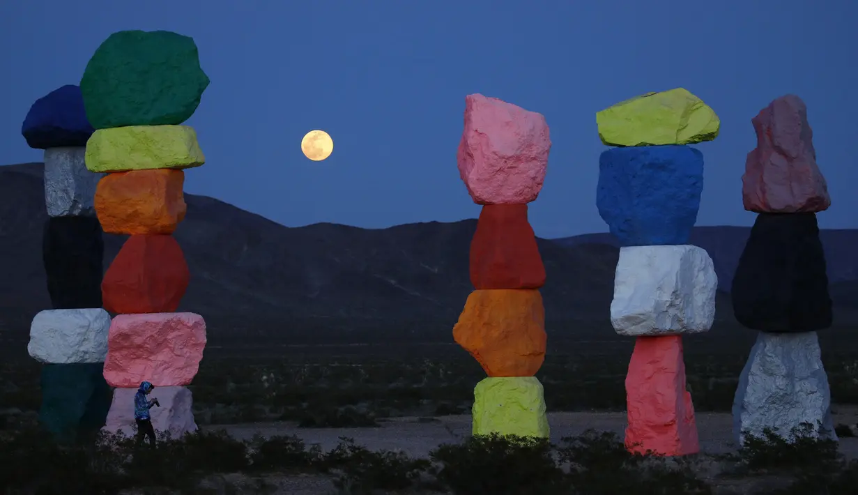 Supermoon terlihat dari celah instalasi seni Seven Magic Mountains karya seniman Ugo Rondinone di Las Vegas, Amerika Serikat, Selasa (7/4/2020). Seven Magic Mountains adalah instalasi seni tumpukan batu setinggi 35 kaki. (AP Photo/John Locher)