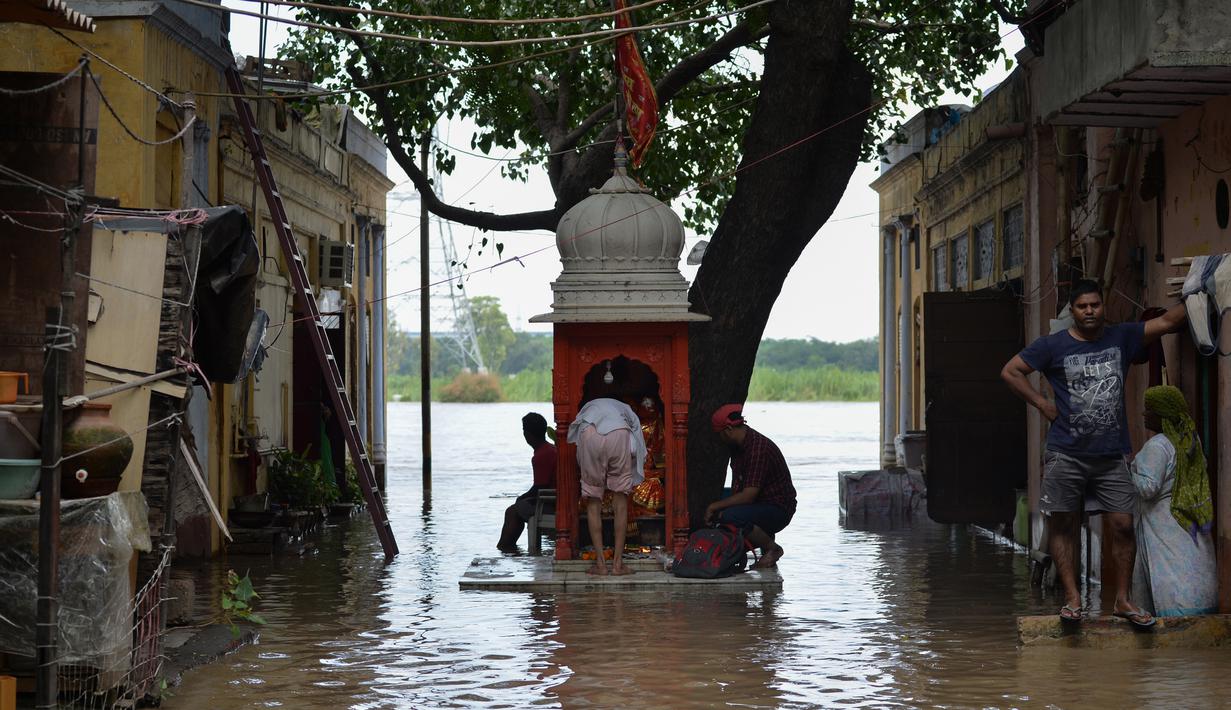 Sejumlah warga berdoa di sebuah kuil kecil saat air membanjiri perumahan dekat tepi Sungai Yamuna yang meluap di New Delhi, India, Selasa (20/8/2019). (AFP Photo/Sajjad Hussain)