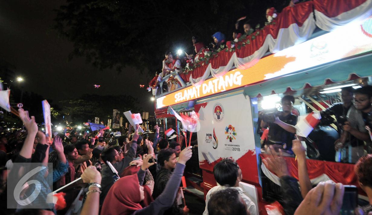 Warga menyambut arak-arakan atlet Indonesia yang berjuang di Olimpiade Rio 2016, Jakarta, Selasa (23/8). Setibanya di Tanah Air, atlet Olimpiade diarak menggunakan bus Bamdros menuju gedung Kementerian Pemuda dan Olahraga. (Liputan6.com/Yoppy Renato)