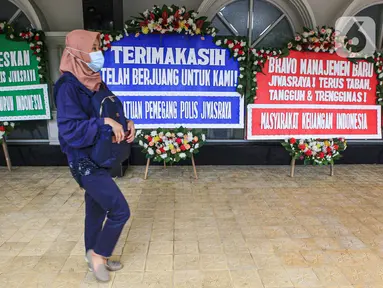 Seorang wanita berjalan dekat karangan bunga di halaman Kantor PT Asuransi Jiwasraya (Persero), Jakarta, Selasa (15/12/2020). Nasabah Jiwasraya ramai-ramai mengirimkan karangan bunga ke Kantor PT Asuransi Jiwasraya (Persero). (Liputan6.com/Faizal Fanani)