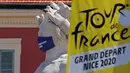 Logo Tour de France 2020 terlihat di dekat patung bermasker di kota Nice, French Riviera, Rabu (26/8/2020). Ajang balap sepeda lintas kota di Prancis kali ini akan dimulai dari kota Nice pada 29 Agustus hingga 20 September di bawah bayang-bayang ‘gelombang kedua’ COVID-19. (Kenzo Tribouillard/AFP)
